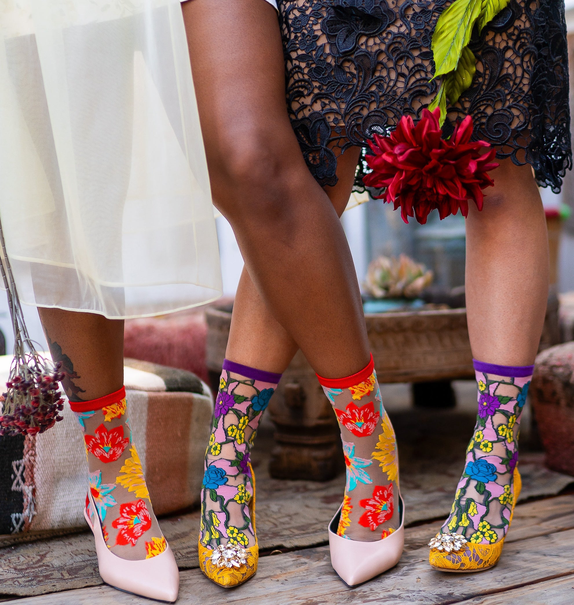 Two models wearing the Sock Candy Garden Party sheer floral socks bundle socks and heels, pictured only from their knees down.