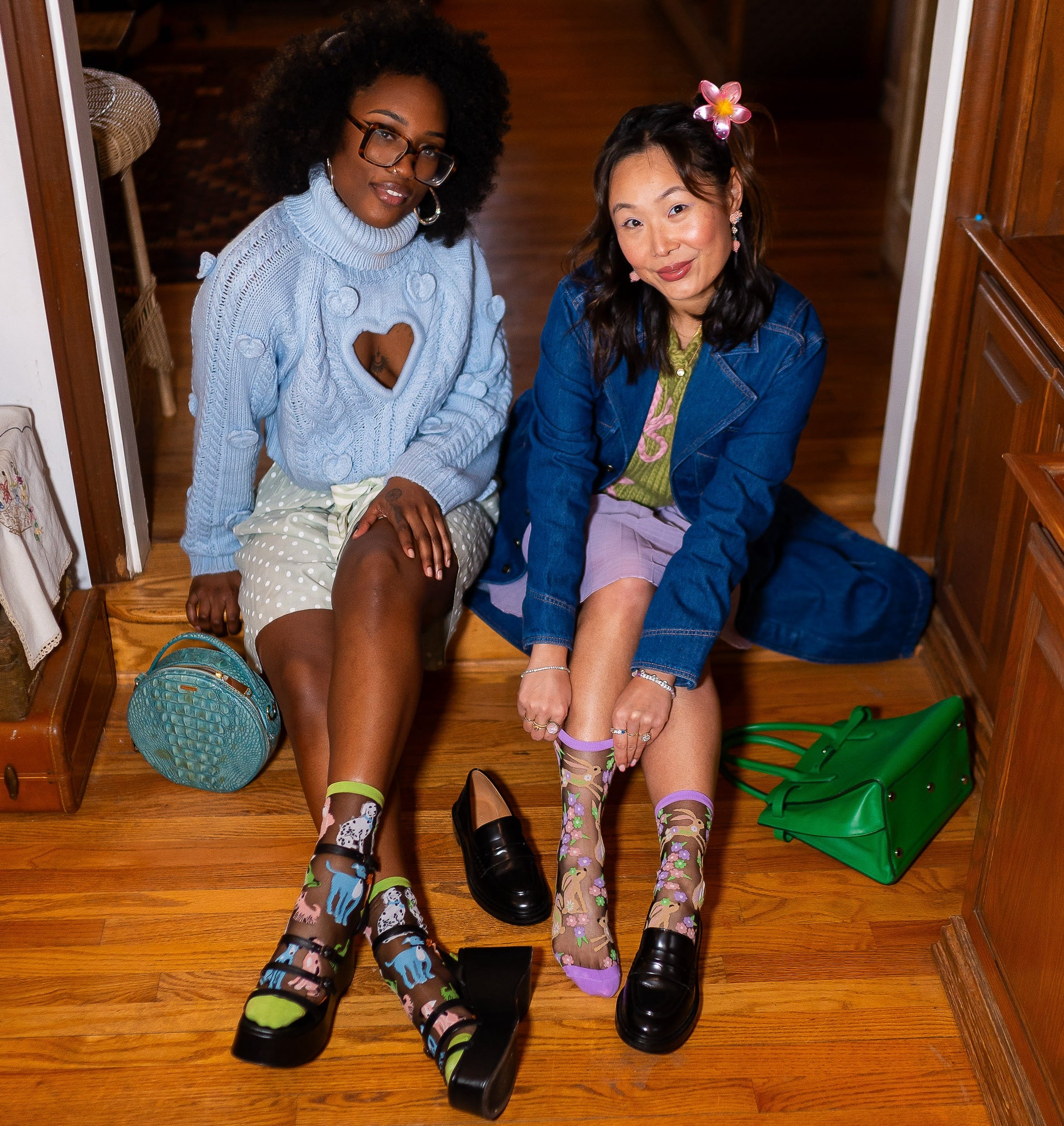 Mary Gui (right) sits on the floor wearing the Sock Candy Animal Lovers sheer sock, with a model (left) sitting next to her wearing another pair of sheer socks.