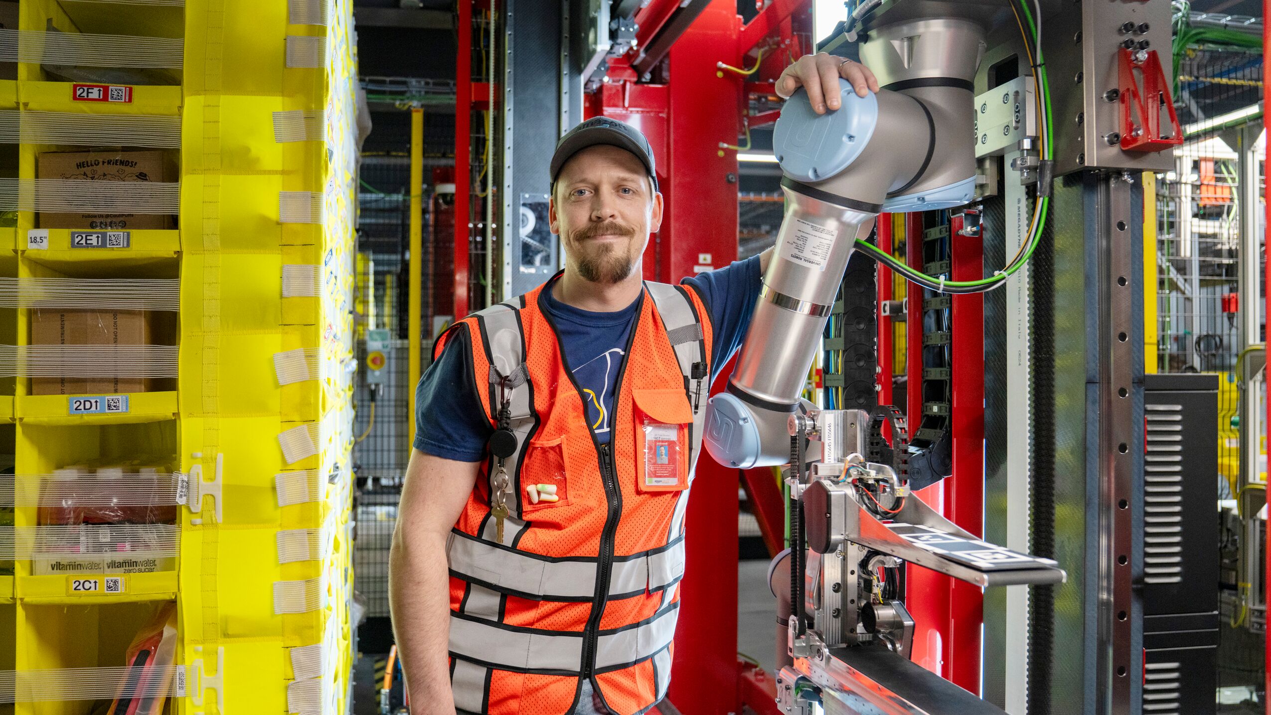 An Amazon fulfillment center employee wearing an orange safety vest with his arm over the Vulcan robotic system