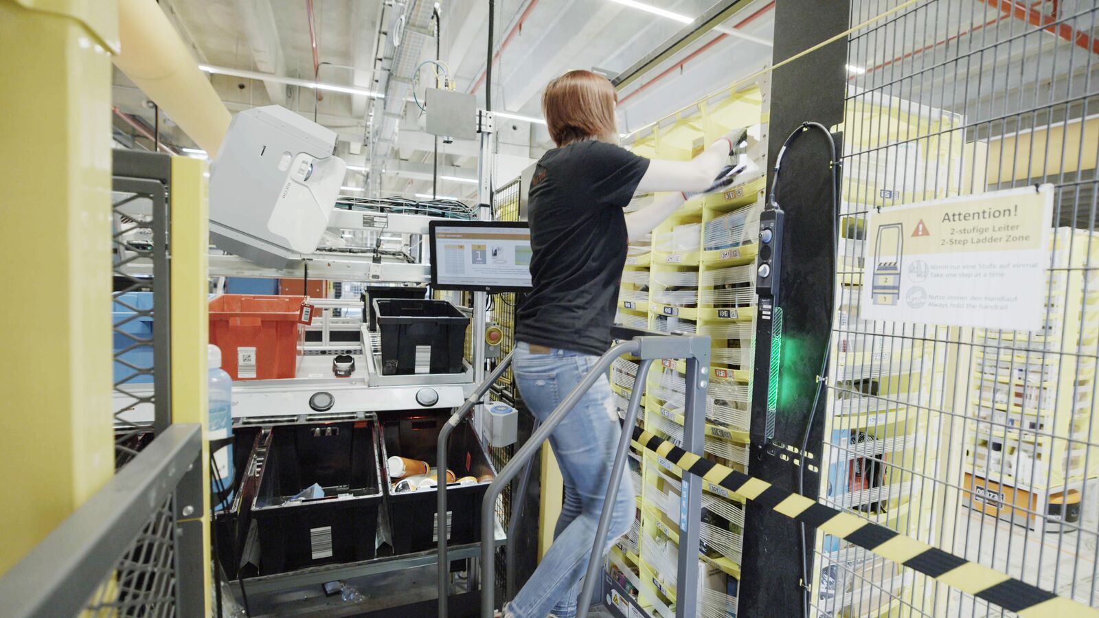 An Amazon fulfillment center employee using a step ladder to place items in the upper part of a storage pod