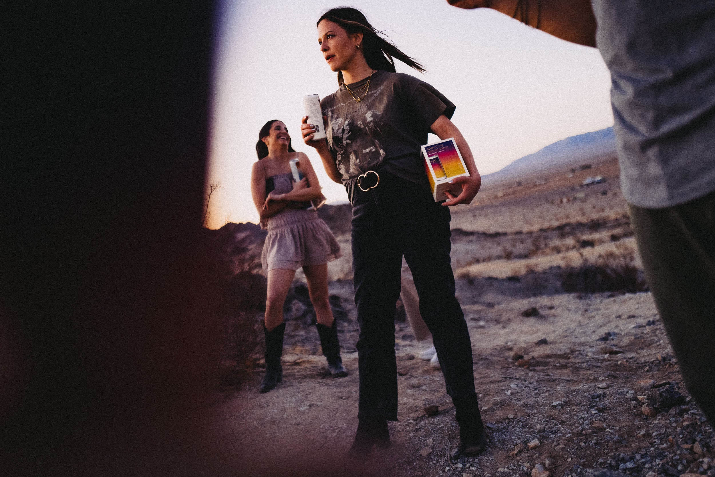 A model poses holding a can of Hiyo with a case of Hiyo in her other hand, in the background she’s joined by more Hiyo drinkers.