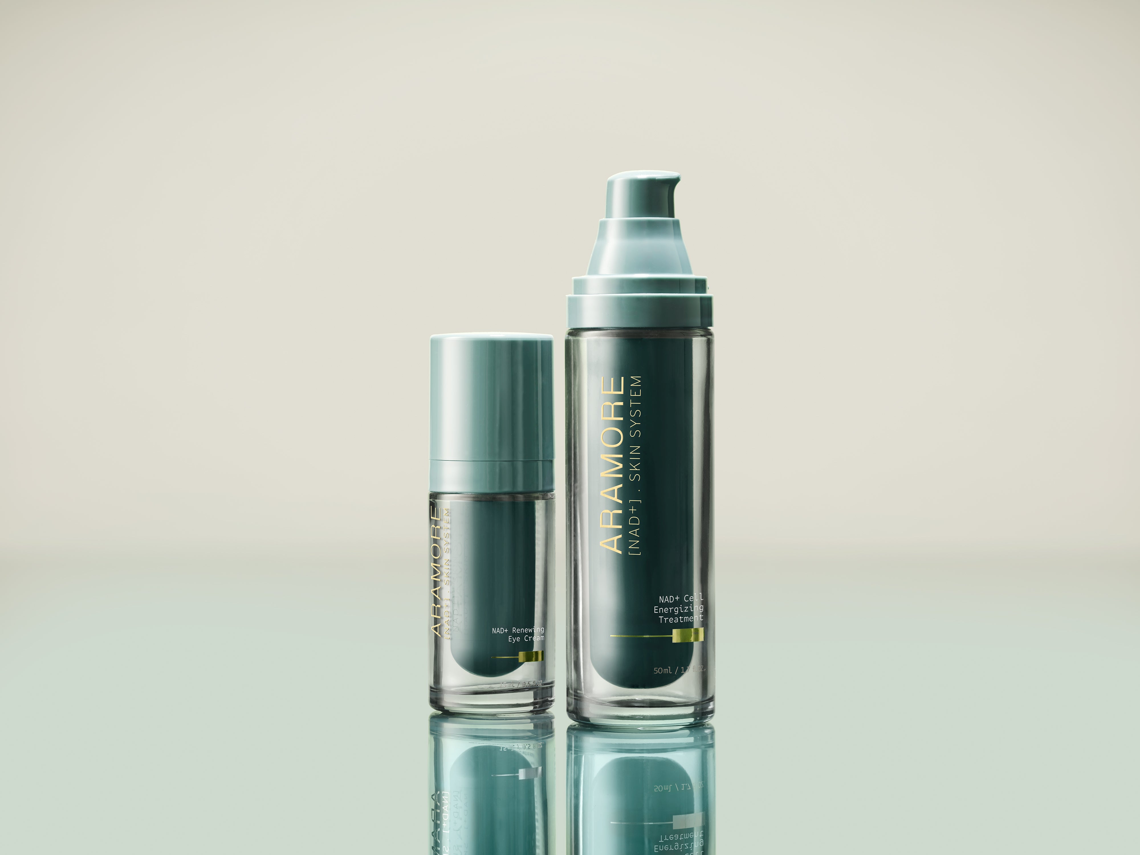 Close-up of two Aramore NAD+ Skin System products — the Renewing Eye Cream and the Cell Energizing Treatment — on a reflective pale green surface.
